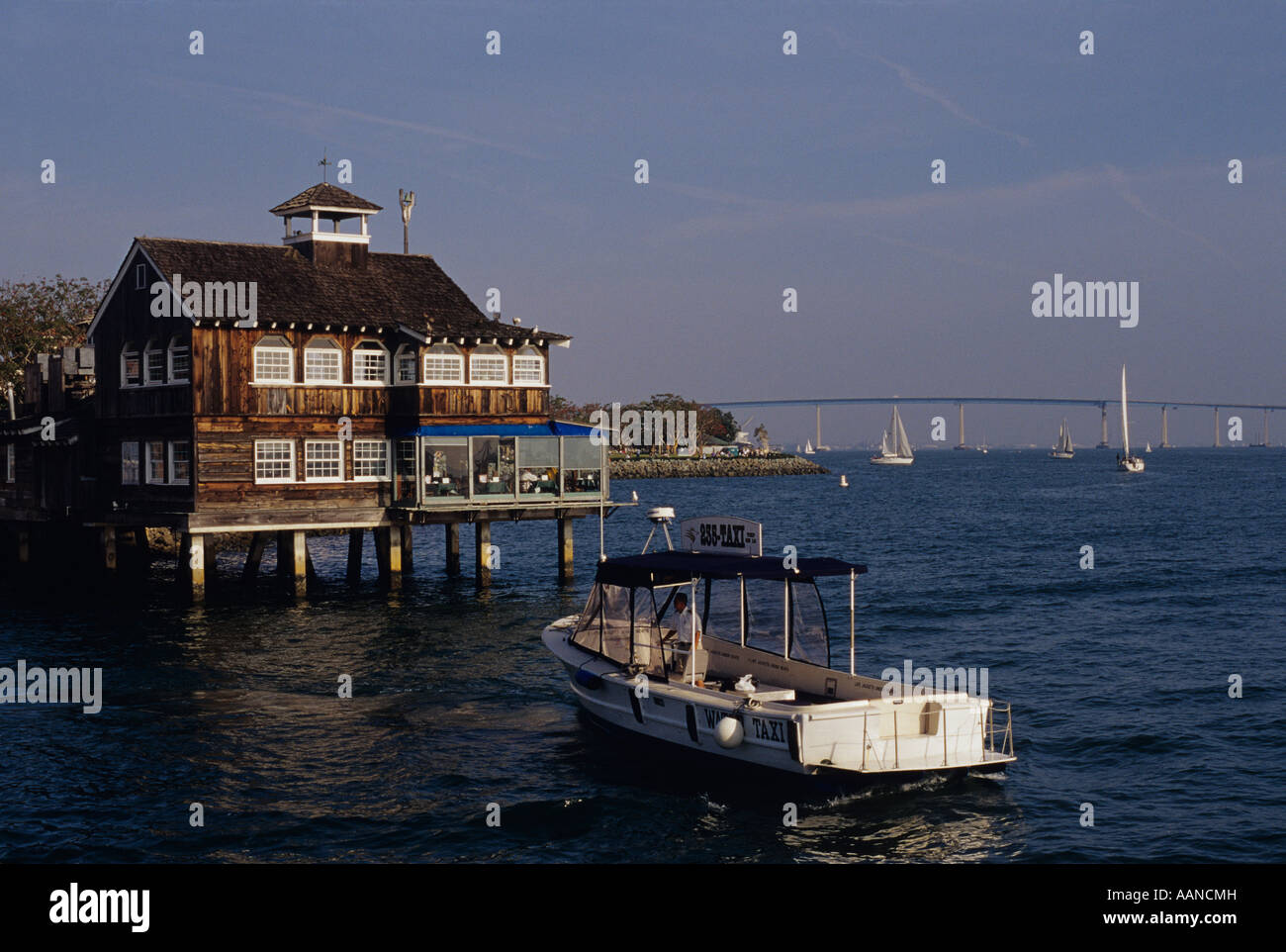 Retro Image SeaPort Village restaurant with water taxi along San Diego bay with sailboats in the background San Diego California USA Stock Photo