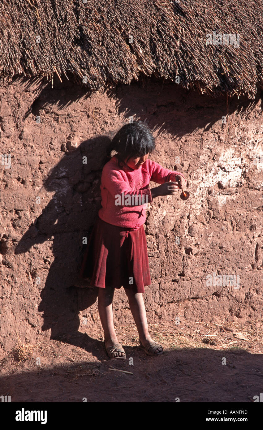 Youngster spinning thread whilst standing against an adobe wall Taquile island Lake Titicaca Peru Stock Photo