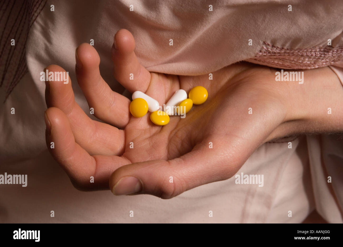 Person on floor under pink duvet showing pills in hand Stock Photo