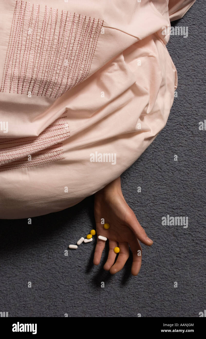 Person on floor under pink duvet showing hand containing pills Stock Photo