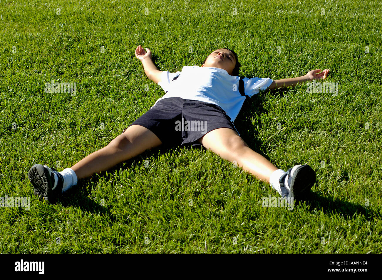 Young boy wearing soccer uniform lying on grass with eyes closed Stock