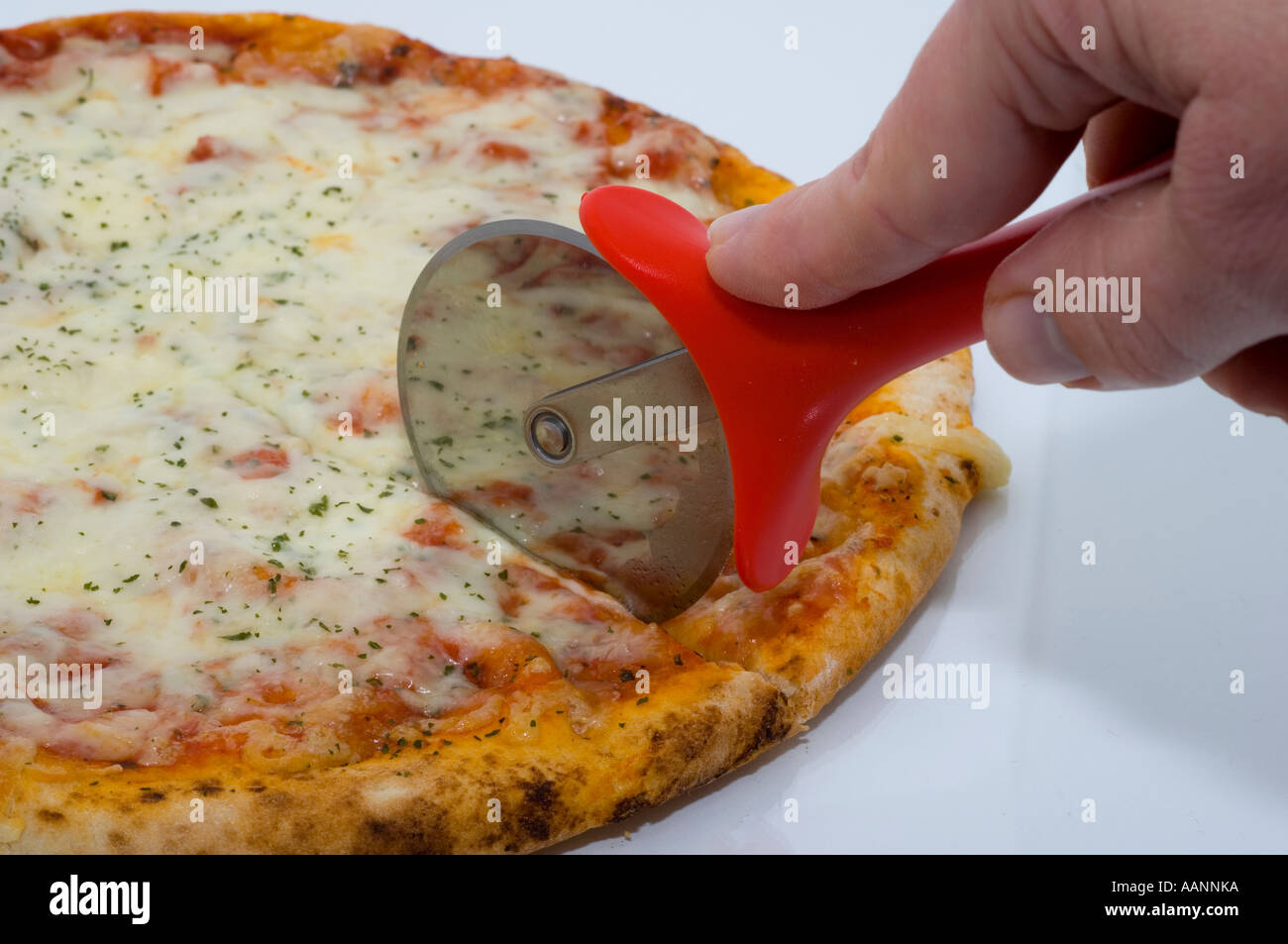 Pizza topped with  cheese and tomato tomato being sliced with a pizza cutter, with reflection in the cutter blade. Stock Photo