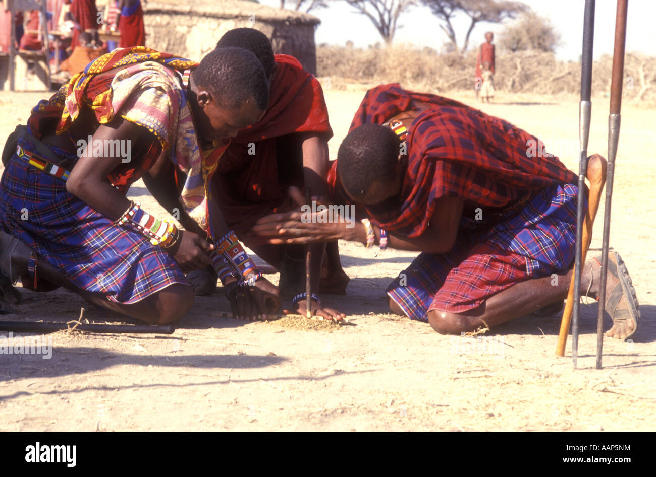 Group of three Maasai men making fire by rubbing sticks together Southern Kenya East Africa Stock Photo