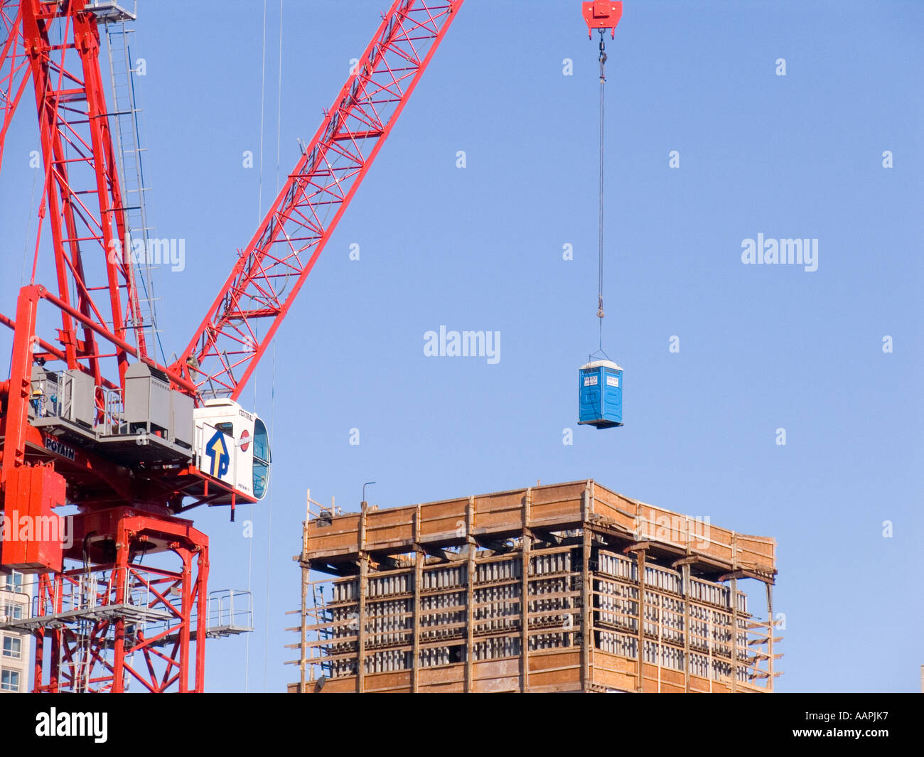 Crane lowering portable lavatory onto construction site Stock Photo