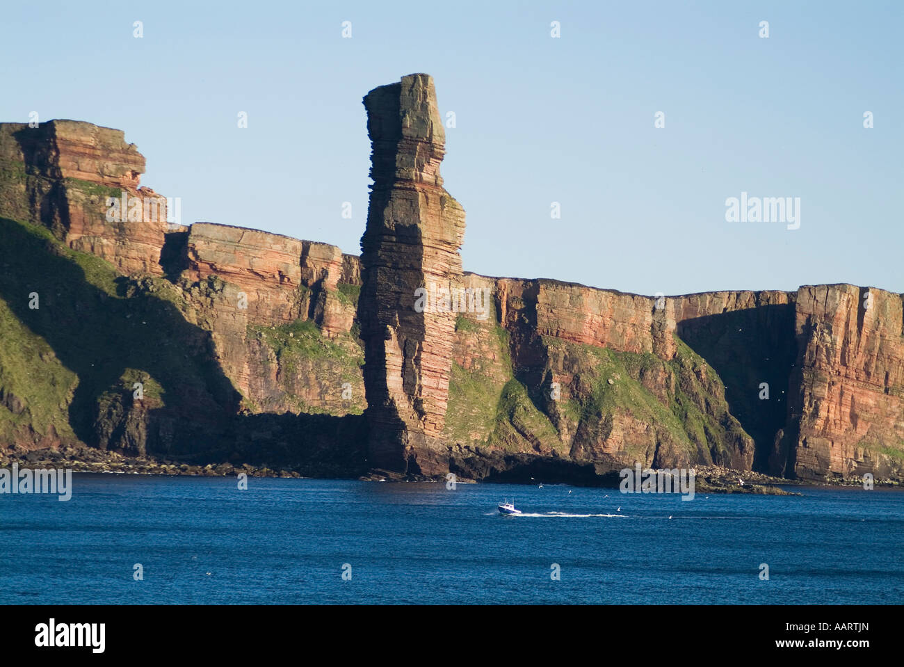 dh Old Man of Hoy HOY ORKNEY Scotland Small boat below Sea stack and seacliffs blue sea cliff rugged landmark boats Stock Photo