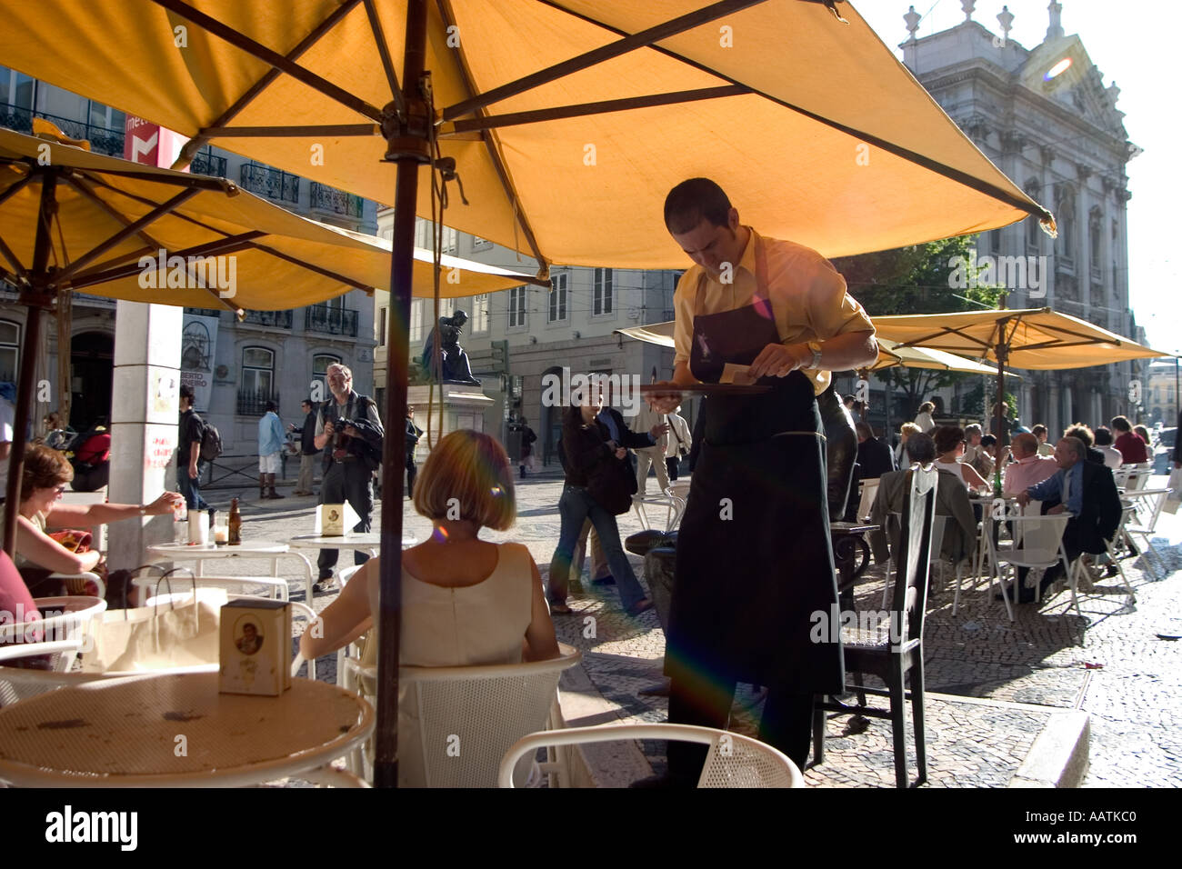 A tall waiter takes an order from a young woman at a sidewalk cafe in Lisbon Portugal Stock Photo