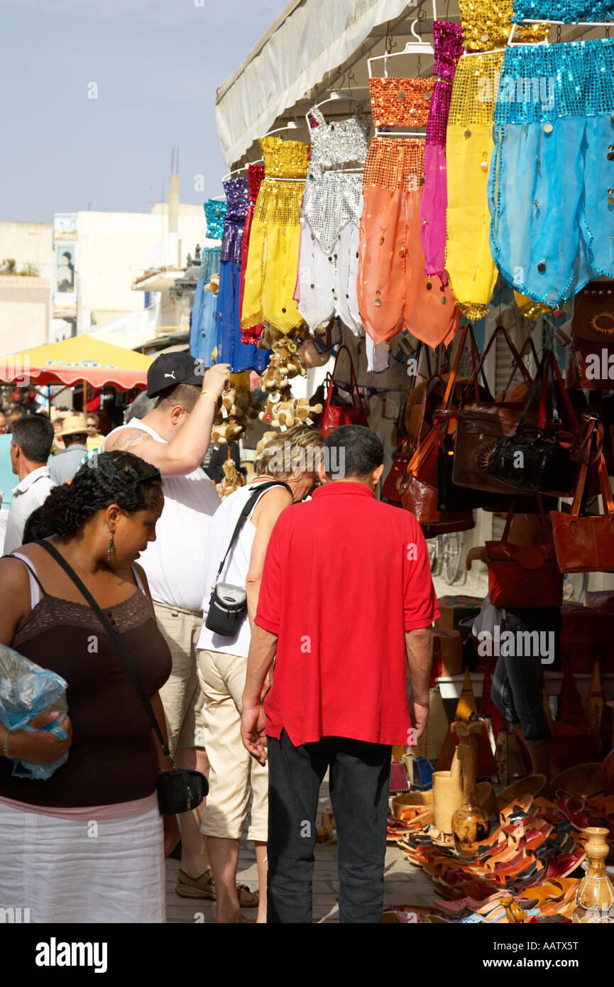 tourists examine items on stall below colourful traditional belly dancer sequined outfits hanging for sale on market stall Stock Photo