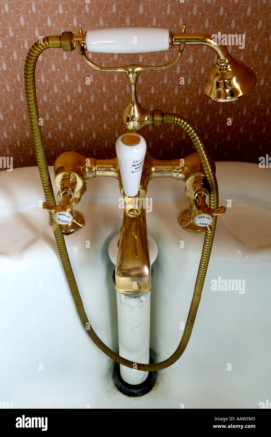 Edwardian brass bath fixture with mixer taps shower attachment and pull up waste plug in bathroom setting with period wallpaper Stock Photo