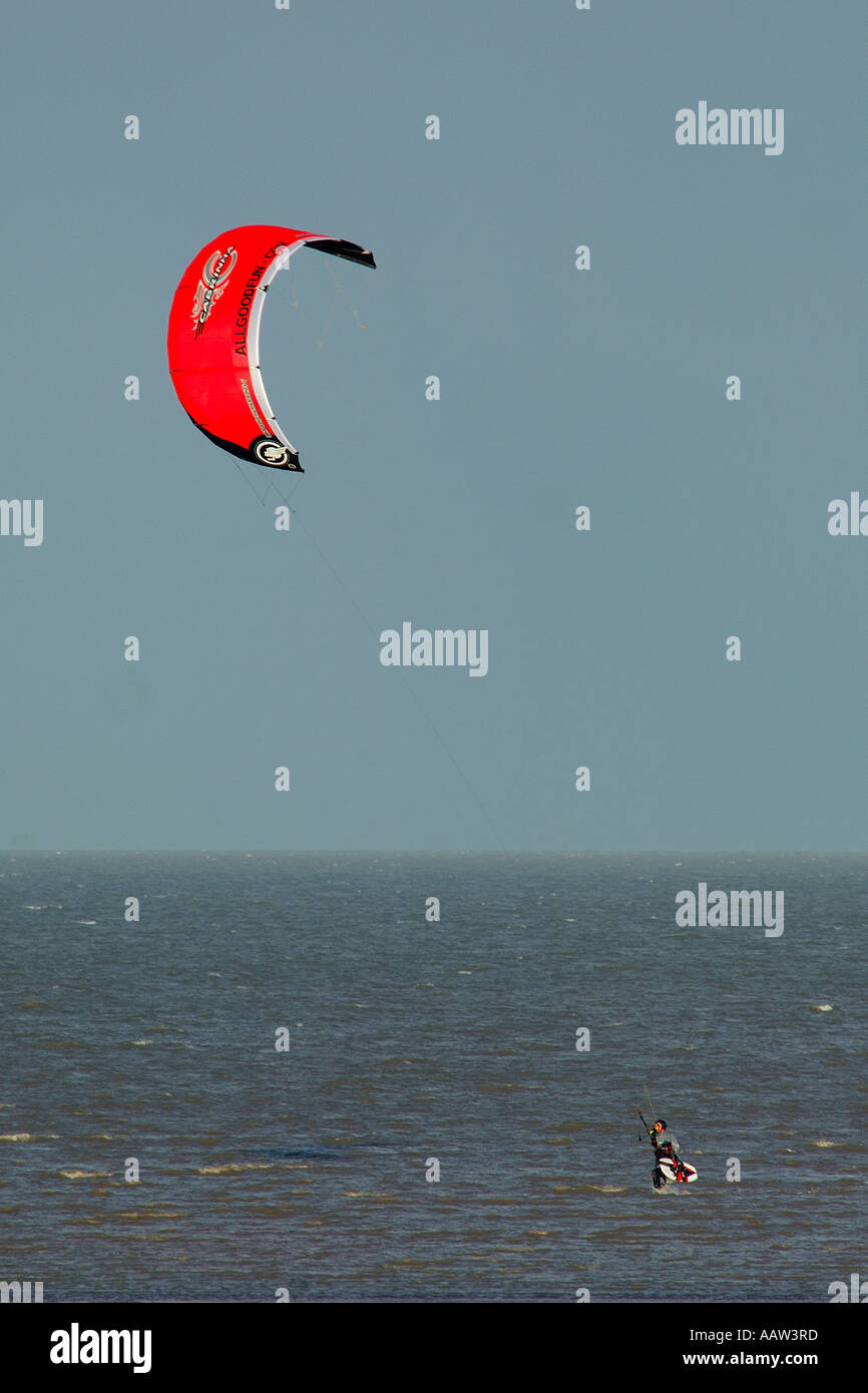 Single kite surfer wading into shore after surfing out to sea with bright red kite poor overcast weather Stock Photo