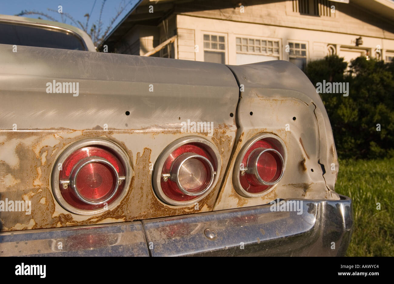 Color horizontal image of the tail of an old Chevy Impala with a bungalow house in the background in warm afternoon light Stock Photo