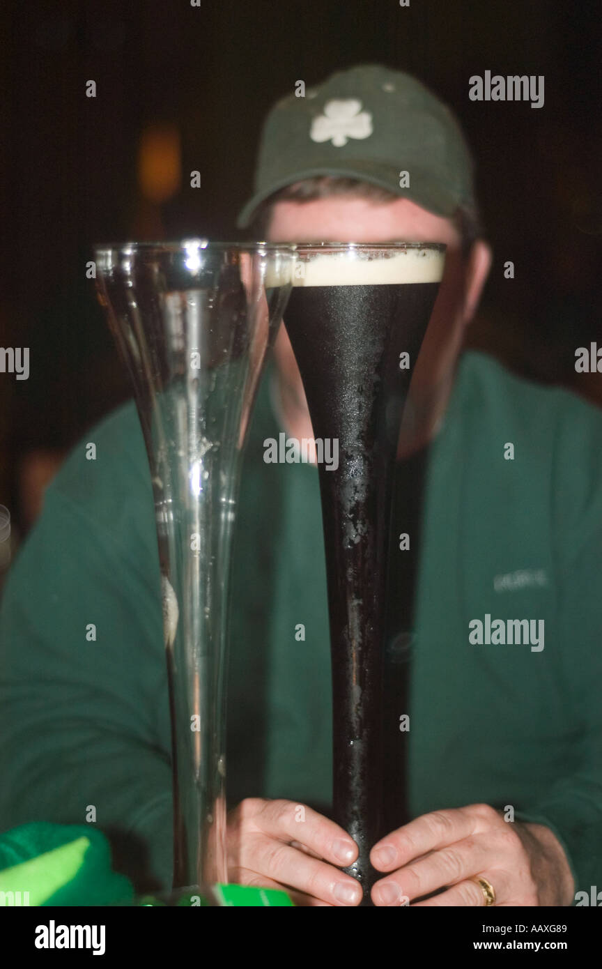 A color vertical image of a chubby caucasian man in a green sweatshirt and shamrock cap hidden behind two half yard beer glasses Stock Photo