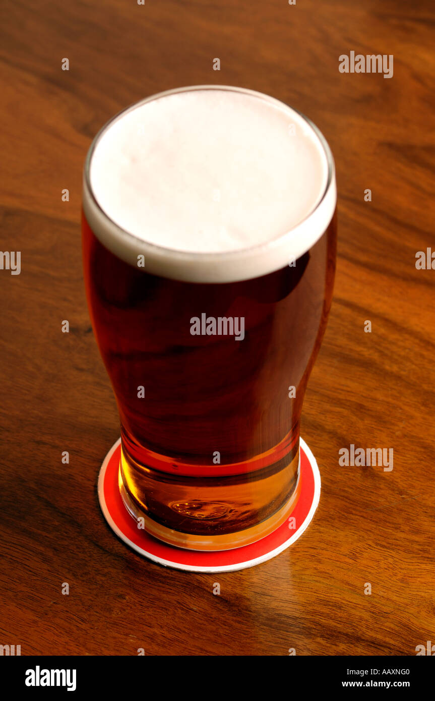 Full pint of beer on a beer mat on a wooden pub table Stock Photo