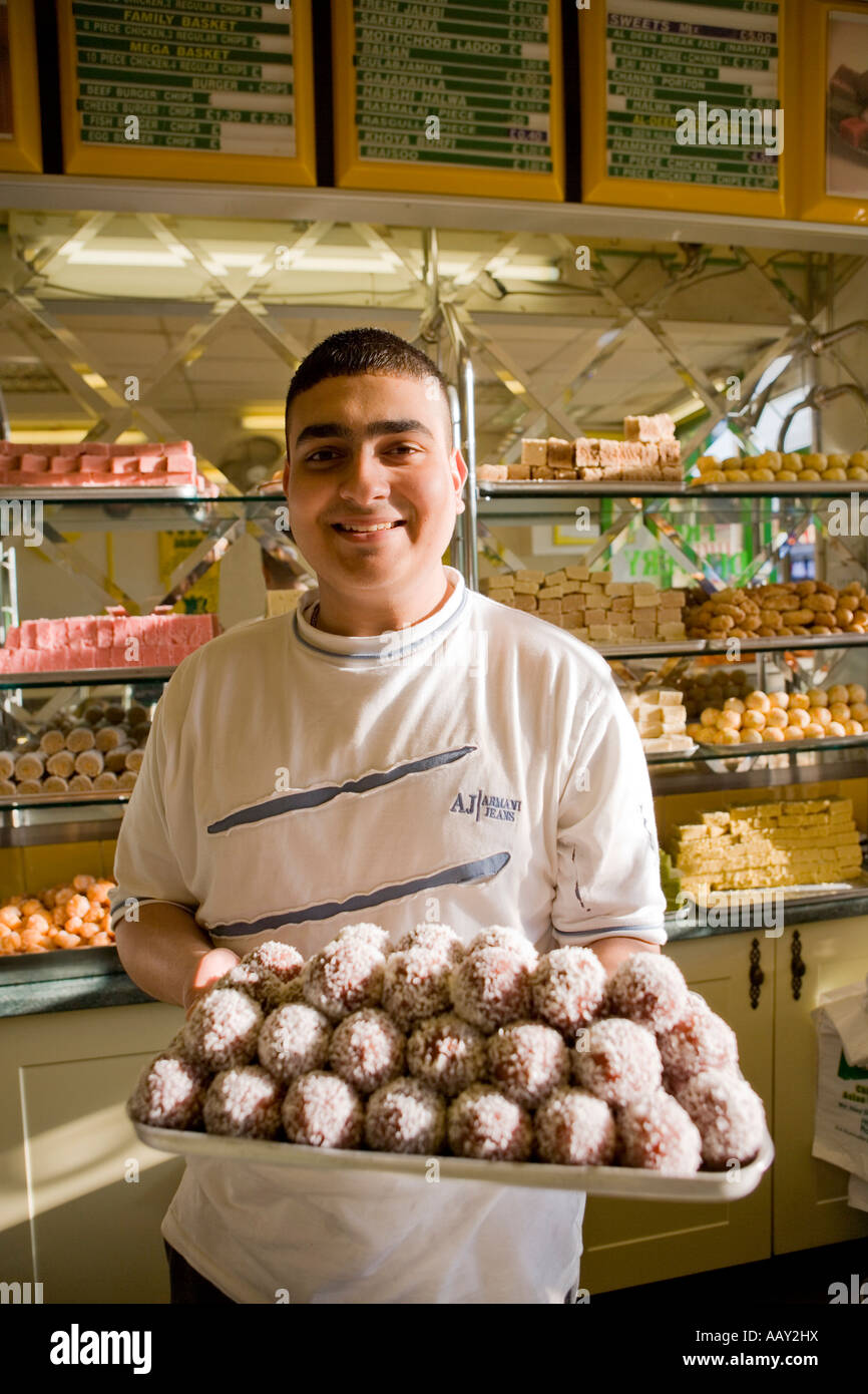 Asian sweet shop owner holding a tray of sweets Luton Bedfordshire UK Stock Photo