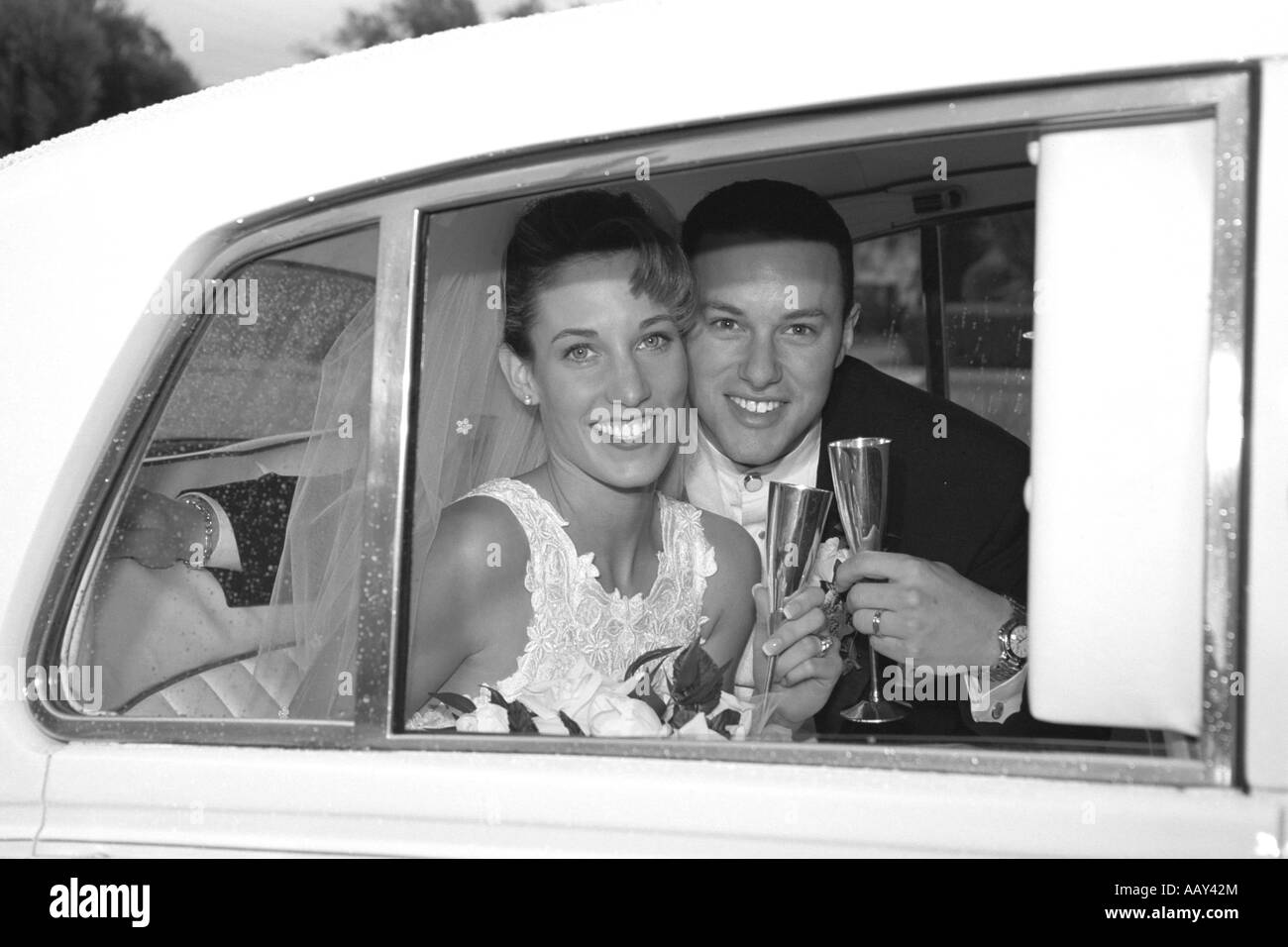 Beautiful bride and groom on happy wedding day in limo toasting glasses black and white horizontal Stock Photo
