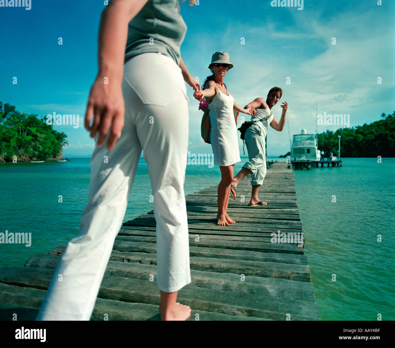 young people on tropical holiday walking on pier to boat Stock Photo