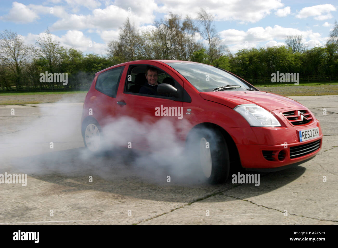A stuntman does a doughnut burnout in a Citroen C2 hatchback car Stock Photo