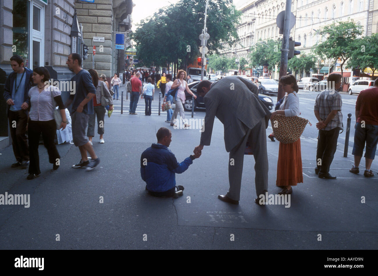 A man leans over to hand some money to a handicapped beggar. Stock Photo