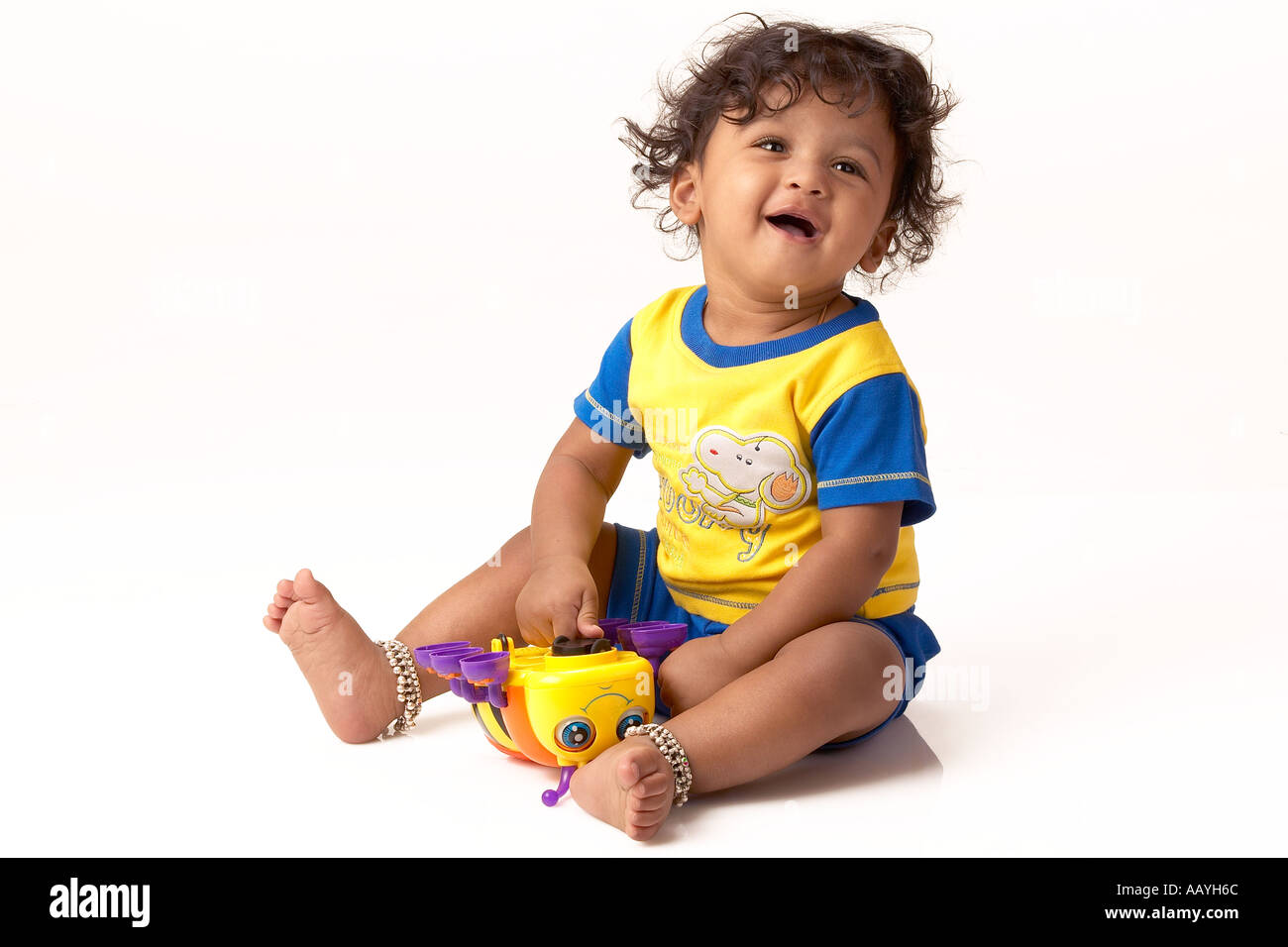 South Asian Indian ten months boy sitting playing with toy curly hair  yellow tee shirt payal in legs Model released number 631 Stock Photo - Alamy