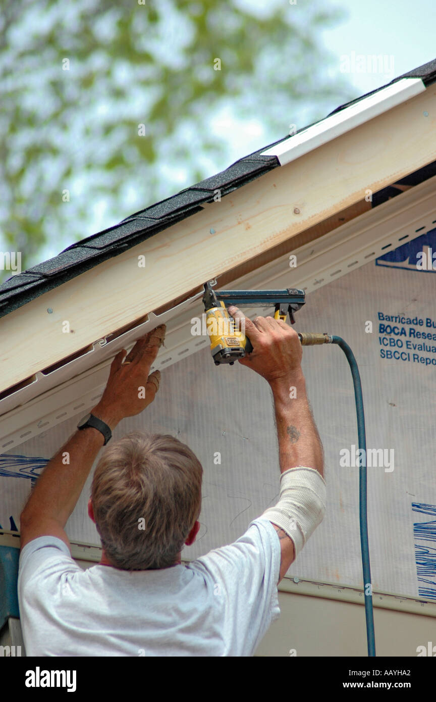Installing vinyl siding on new home construction on ladder and using