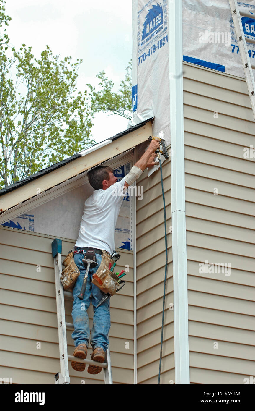 Installing vinyl siding new home construction on ladder using nail gun chop saw tape measure