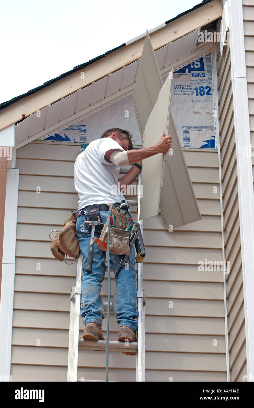 Installing vinyl siding new home construction on ladder using nail gun