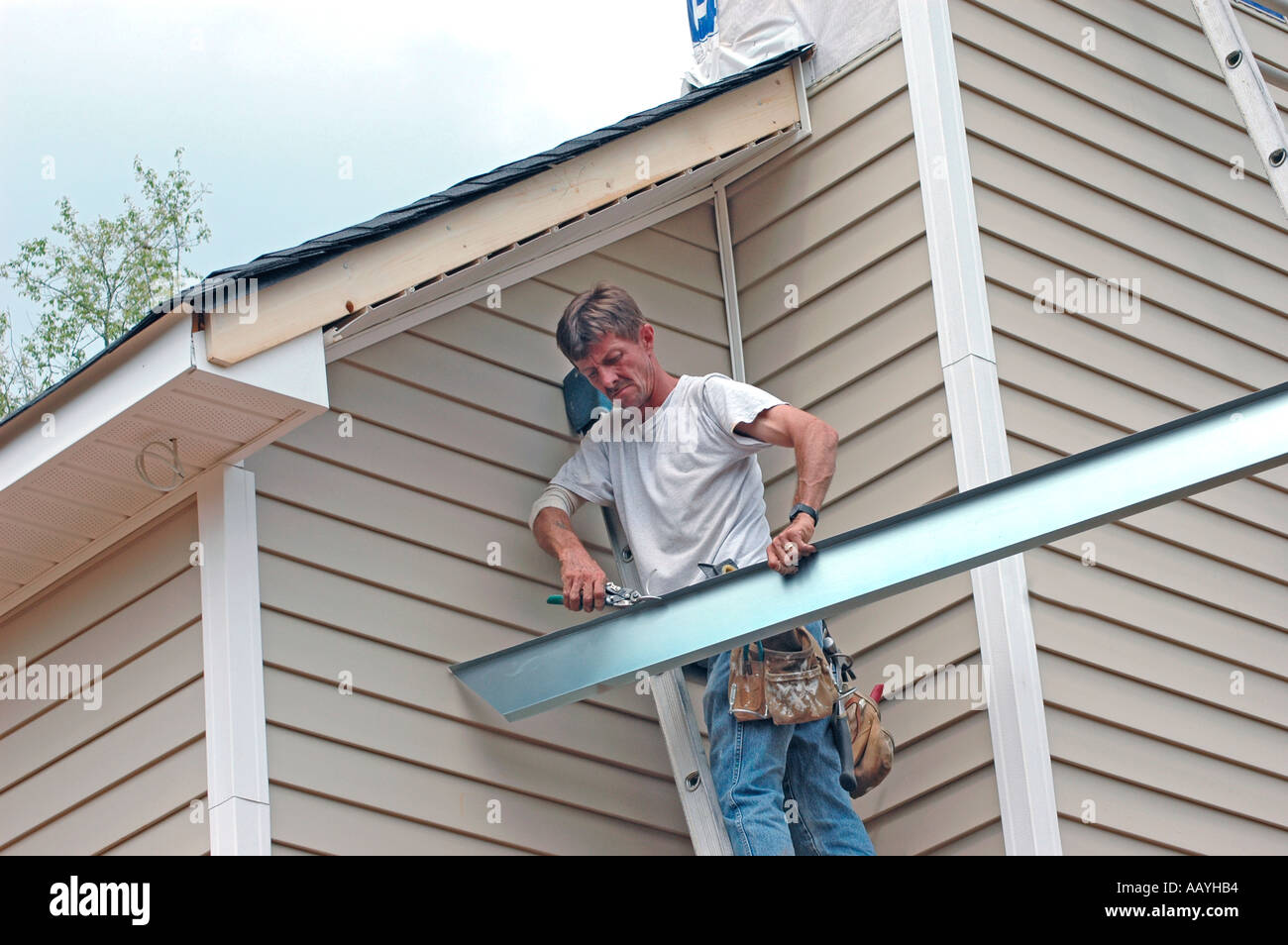 Installing vinyl siding new home construction on ladder using nail gun chop saw tape measure