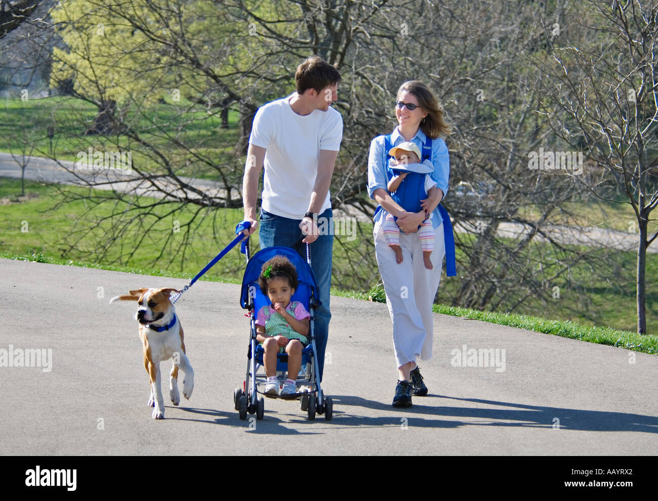 Young Family Walking in Park With Young Daughter in Stroller Baby in