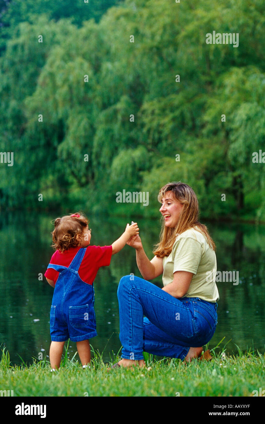 Young Mother Playing with Her Young Daughter Beside Pond Stock Photo