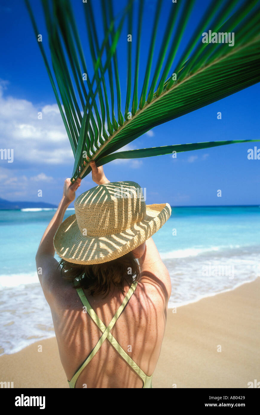 Woman on beach using palm frond leaf for shade Lombok Island Indonesia Southeast Asia Model released image Stock Photo