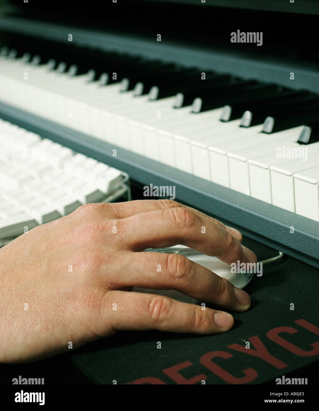 Close up of hand and mouse next to computer and musical keyboard Stock Photo