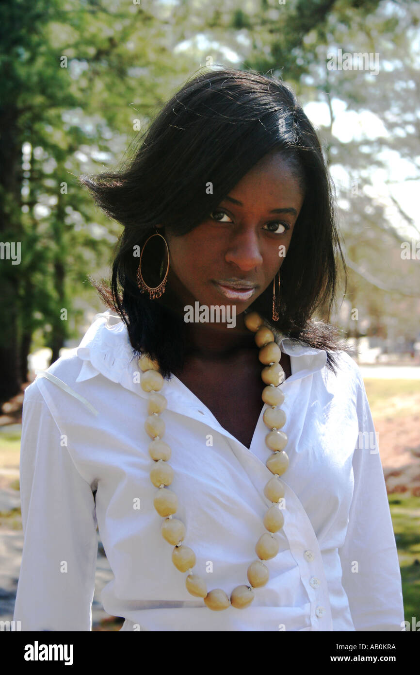 African American woman early 20s with wooden neckless and white blouse, slight turn, face down meek expression. Stock Photo