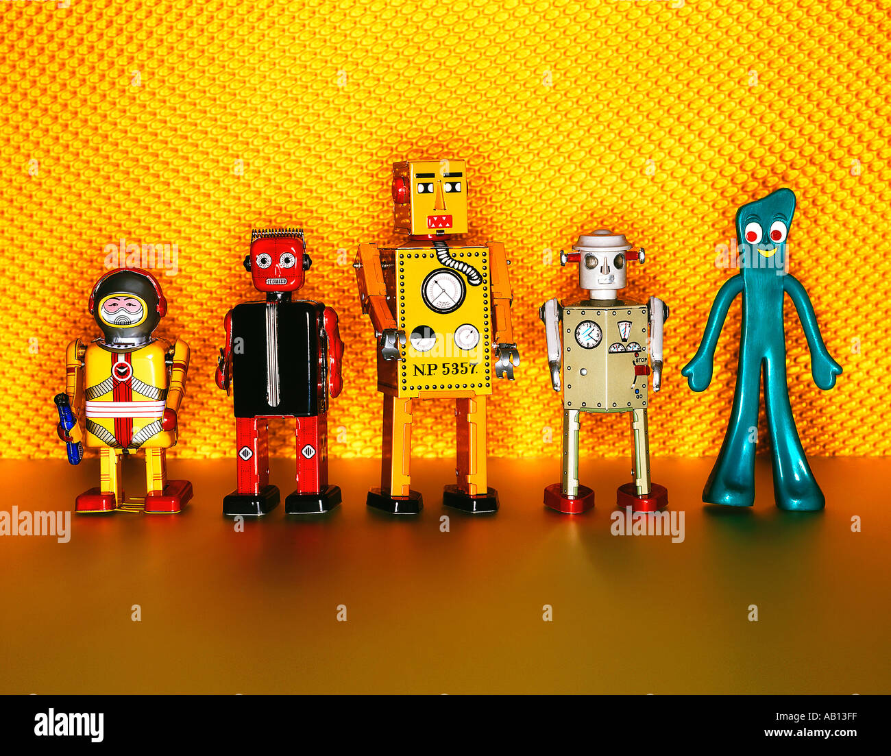 four tin robots and Gumby all in a line on yellow background Stock Photo