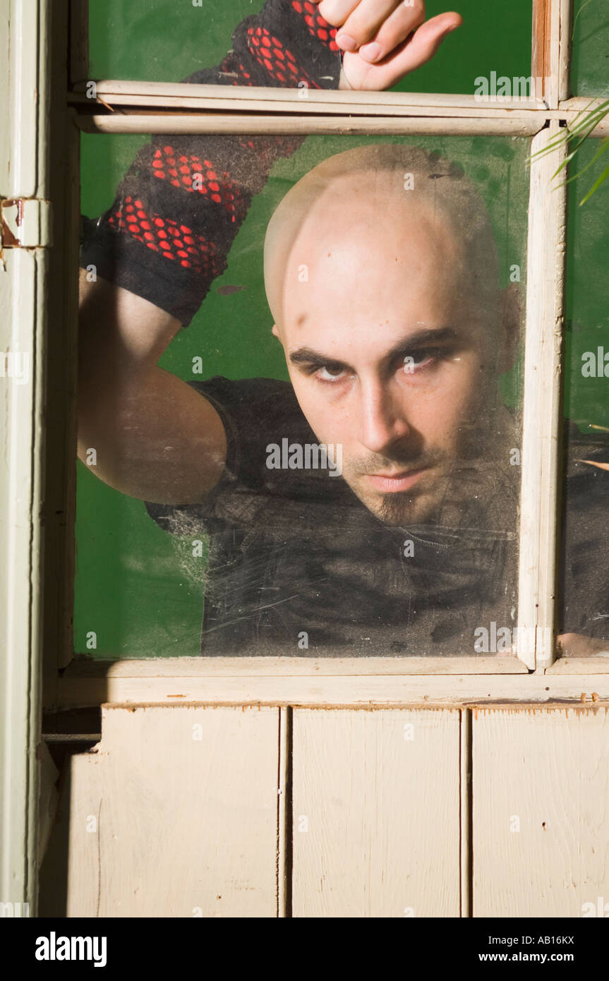 Sinister character peering through a broken window Stock Photo