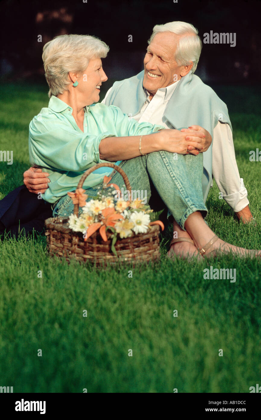 Mature couple sitting on lawn with basket of flowers Stock Photo