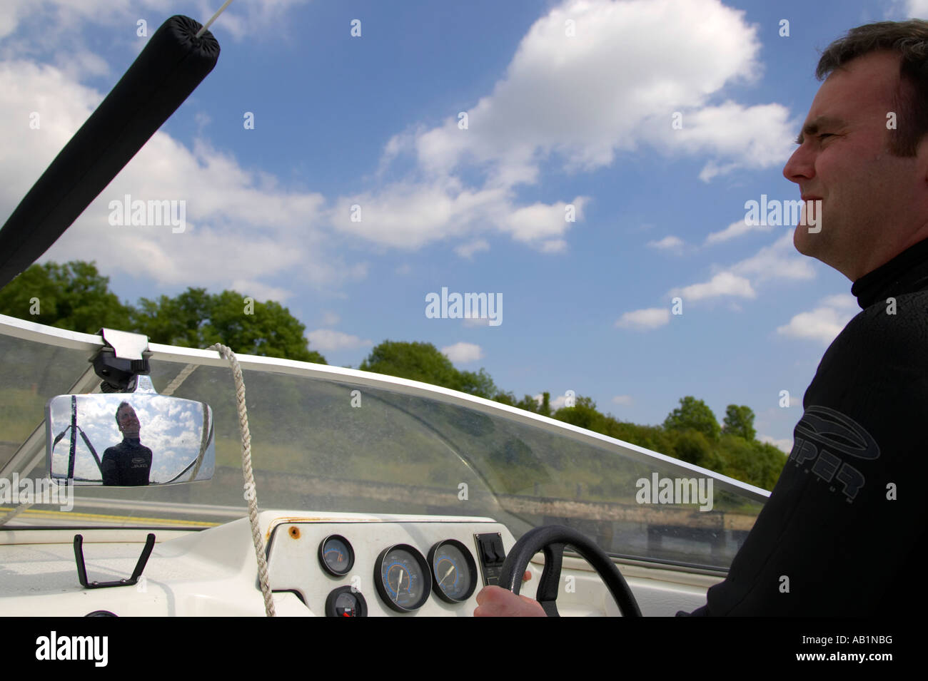early 30s dark haired man driving speedboat during waterski session with blue cloudy sky looking front Stock Photo