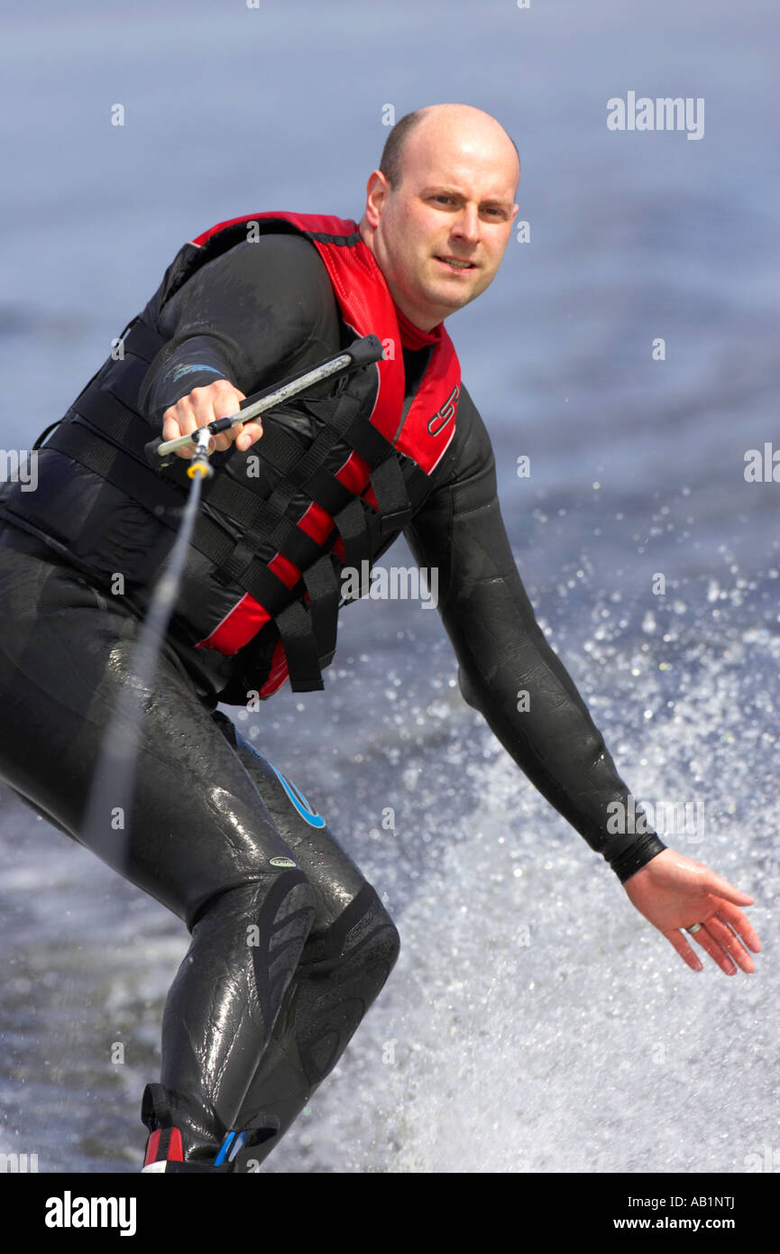 mid 30s male in wetsuit waterskiing balancing on board holding on with one hand with the other in the water splash Stock Photo