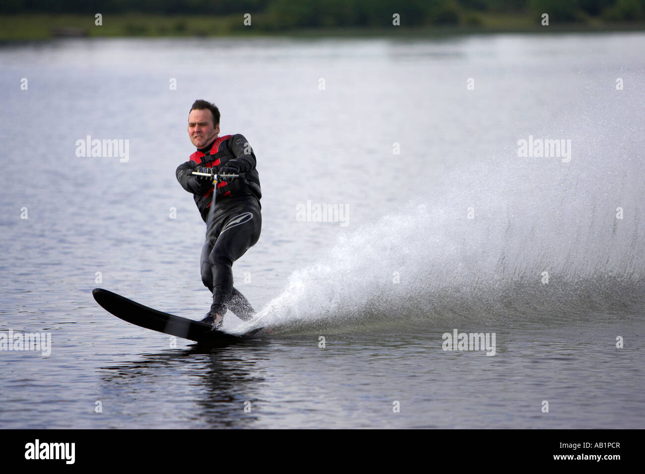 mid 30s man waterskiing on a hard fast cut and turn on one ski throwing