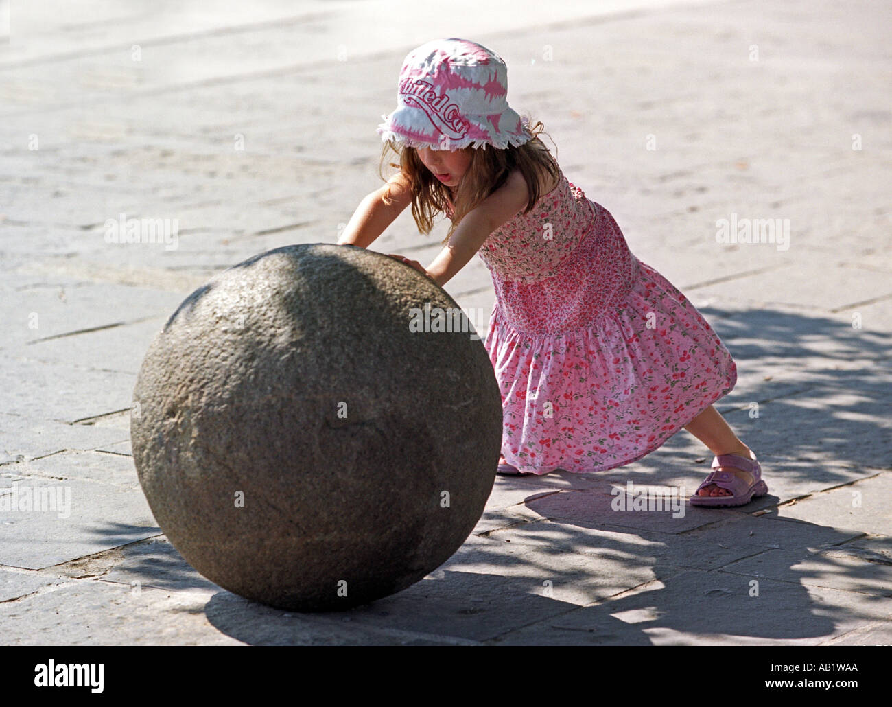 A young girl pushing a large cannonball Stock Photo