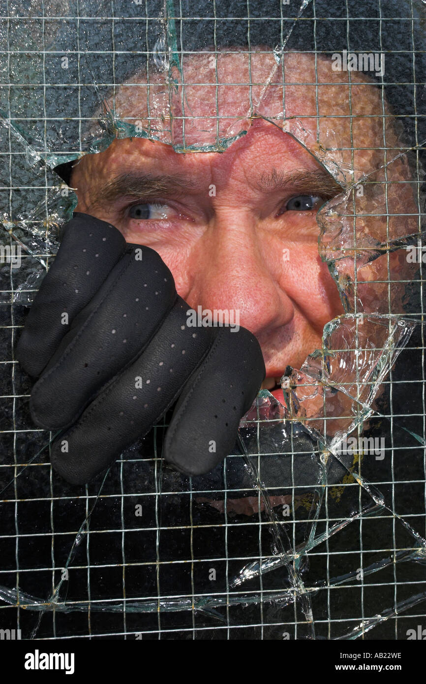 Burglar peering into private property by smashing through wire enforced glass pane. Stock Photo