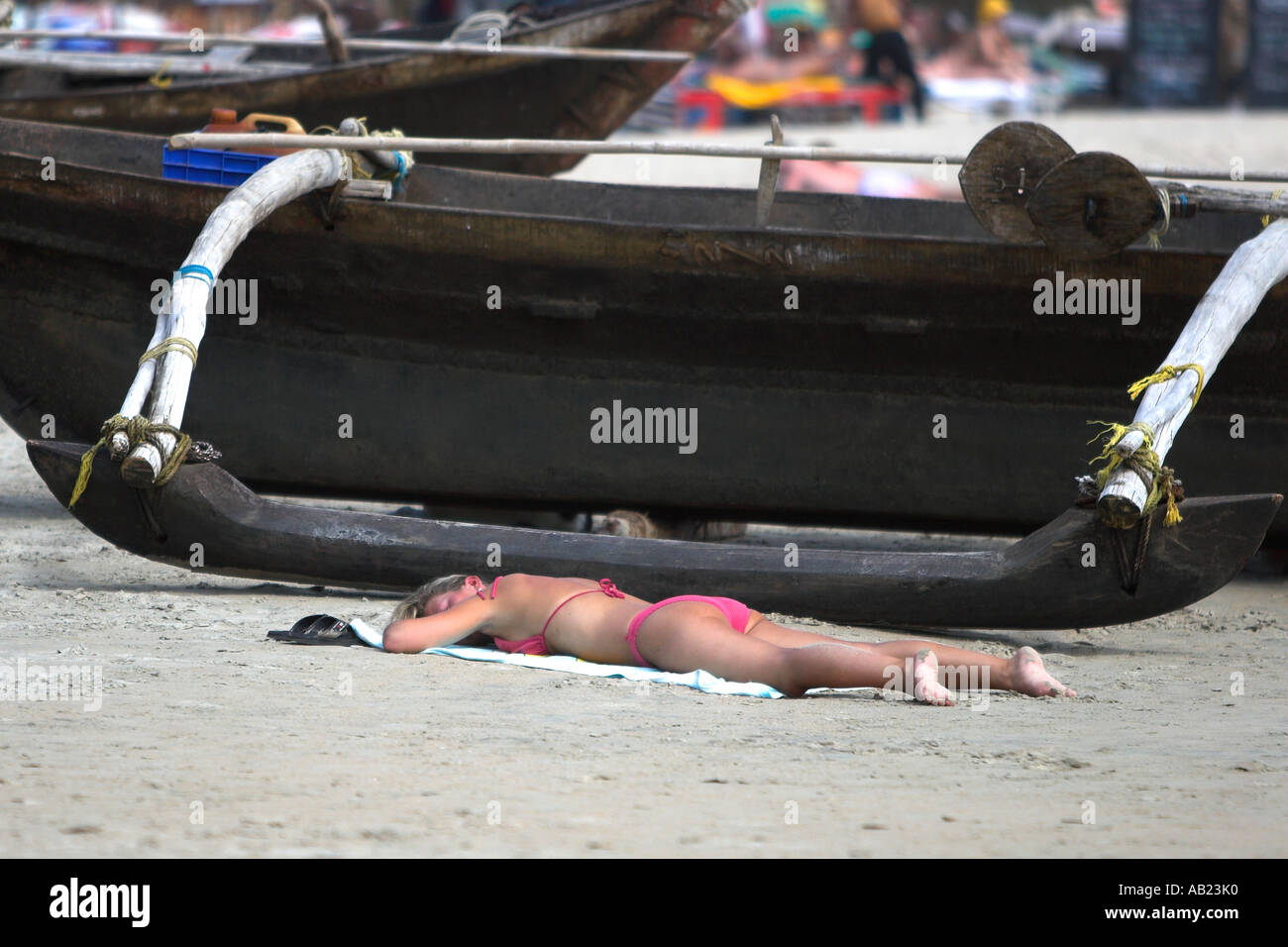 Pink bikini woman sunbathing on beach beside open outrigger boat Palolem south Goa India Stock Photo