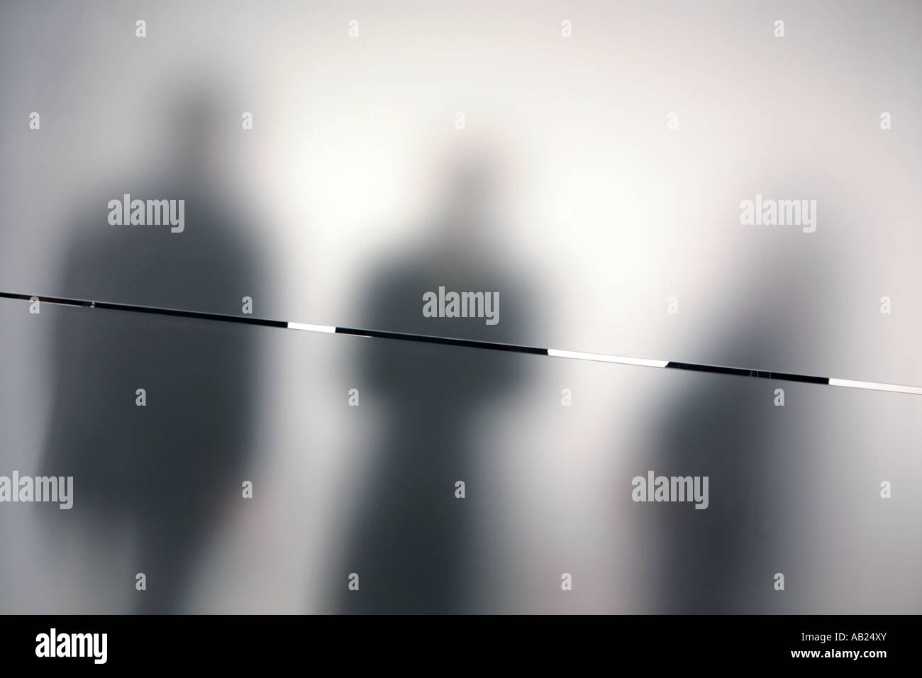 3 shadows behind a calandered glass wall 3 schemenhafte Personen hinter einer satinierten Glaswand Stock Photo