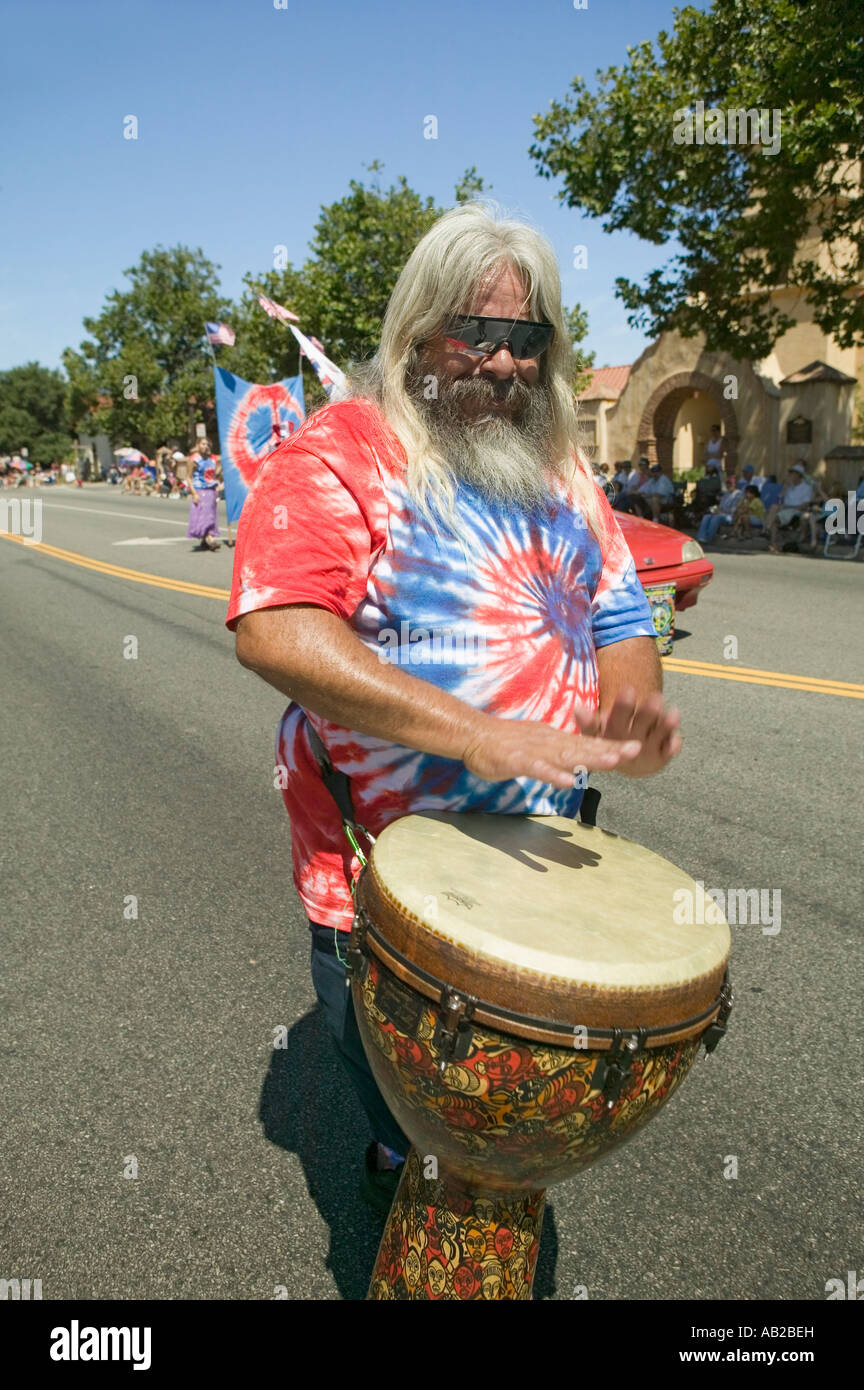 Hippie in red white and blue tie dye t shirt pounds his drum down main street during a Fourth of July parade in Ojai CA Stock Photo