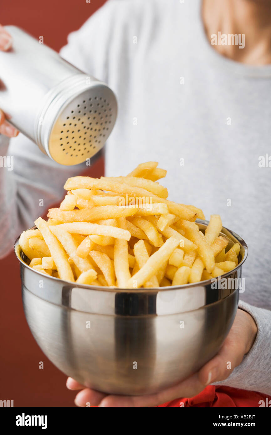 Putting salt on chips in a bowl FoodCollection Stock Photo