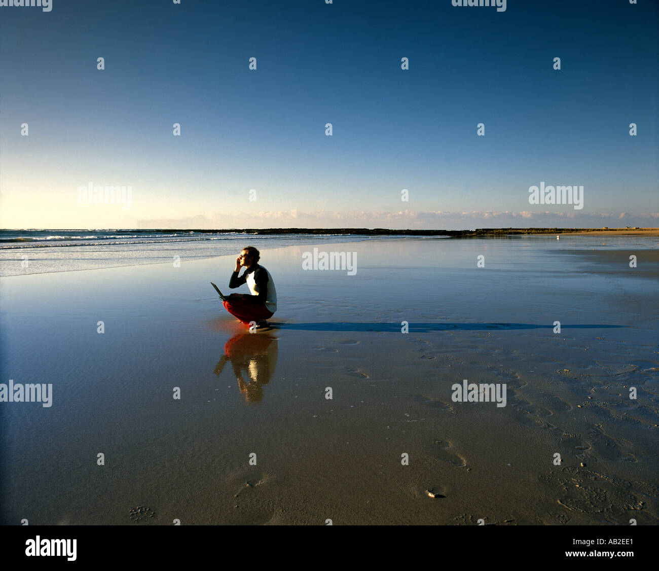 Man on empty beach with laptop computer and mobile phone Stock Photo