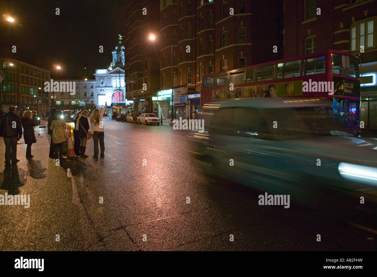 Hailing a cab on wet night streets of West End of London s theater district with double decker bus driving by England Stock Photo