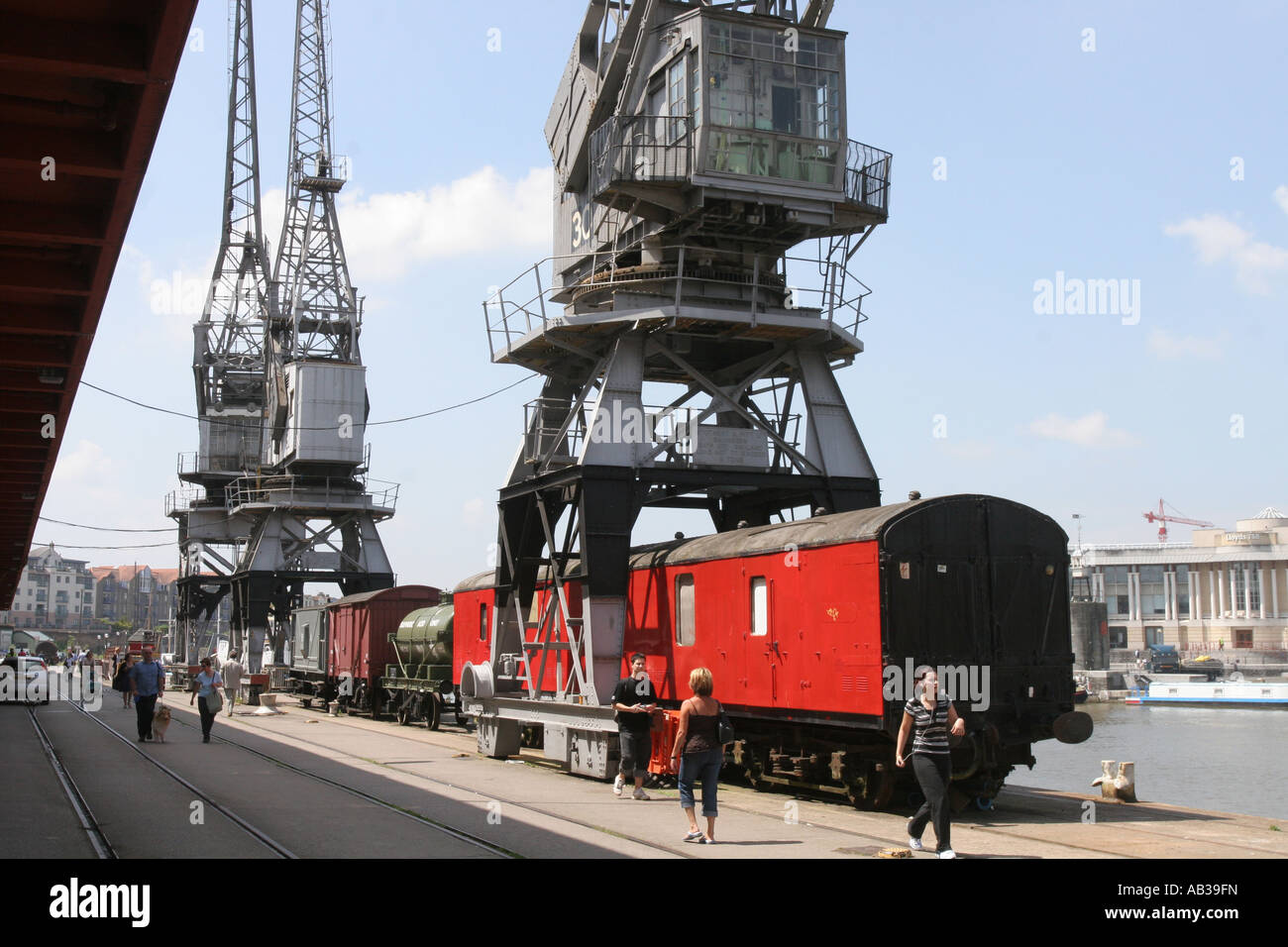 Bristol docks have been regenerated. Old cranes and a  train have been left by the bank as pedestrians pass. Stock Photo
