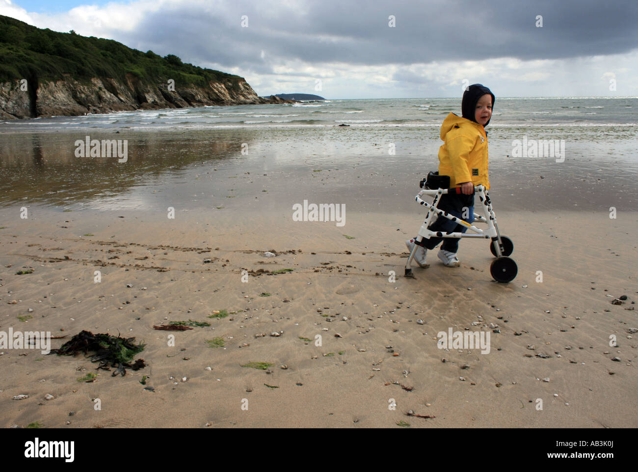 Disabled boy walking with the aid of a Kaye walker on a beach in bad