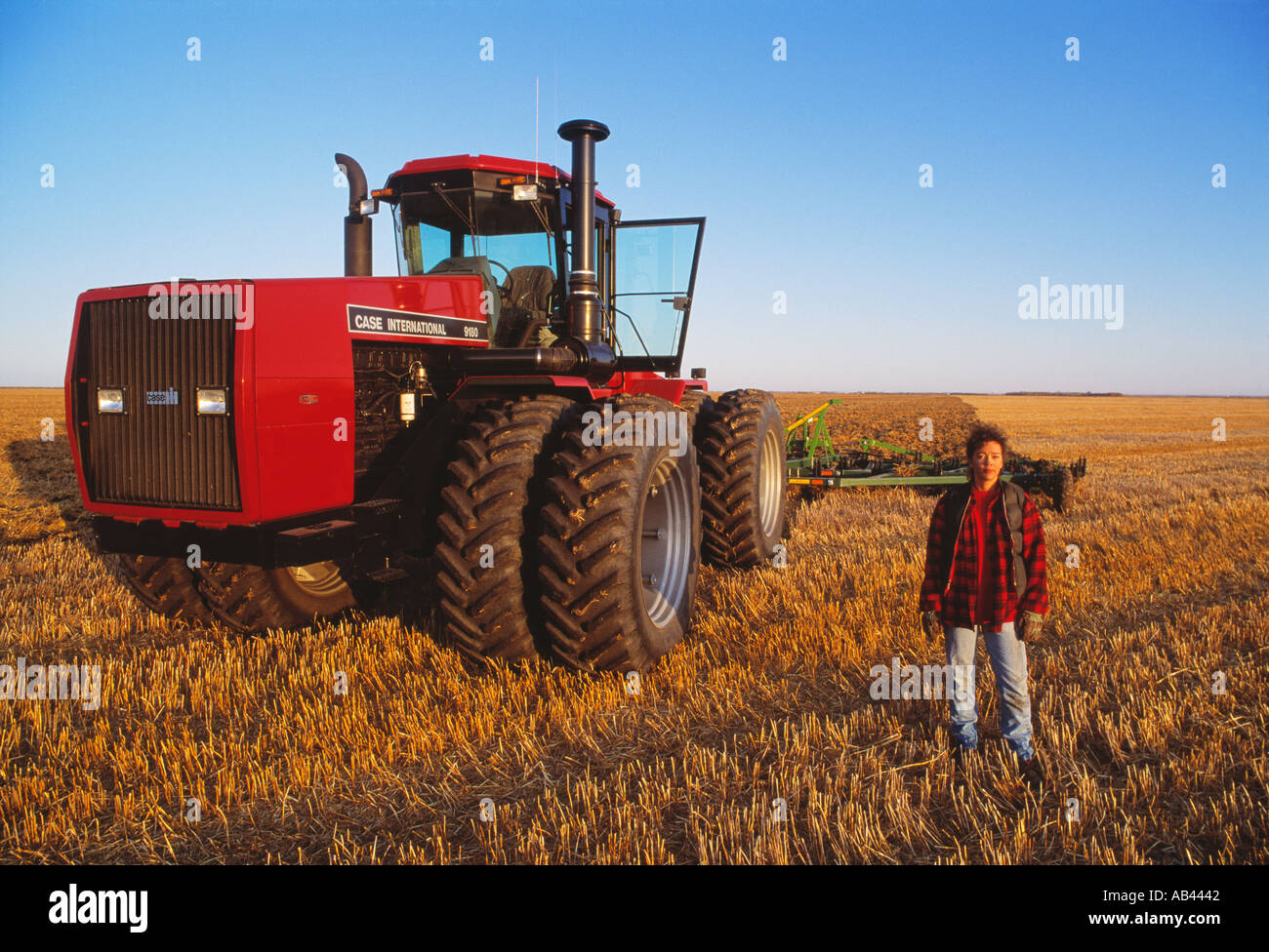 Agriculture - A woman farmer posing with a large tractor and field implement during field preparation operations / Manitoba. Stock Photo
