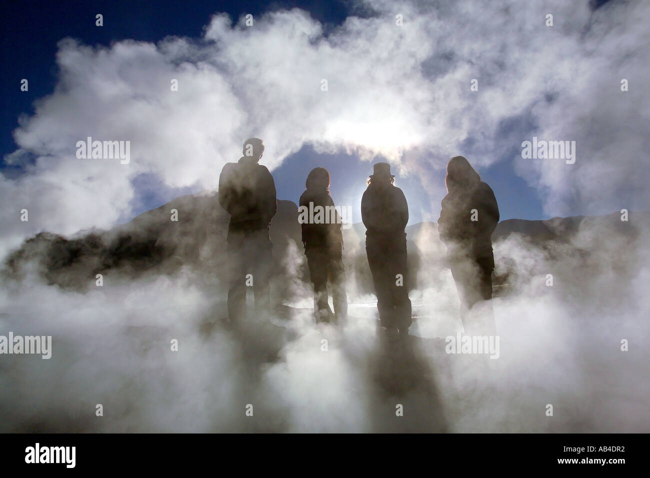 Four tourists silhouetted among the steam from the geysers at El Tatio in the early morning sun. Stock Photo