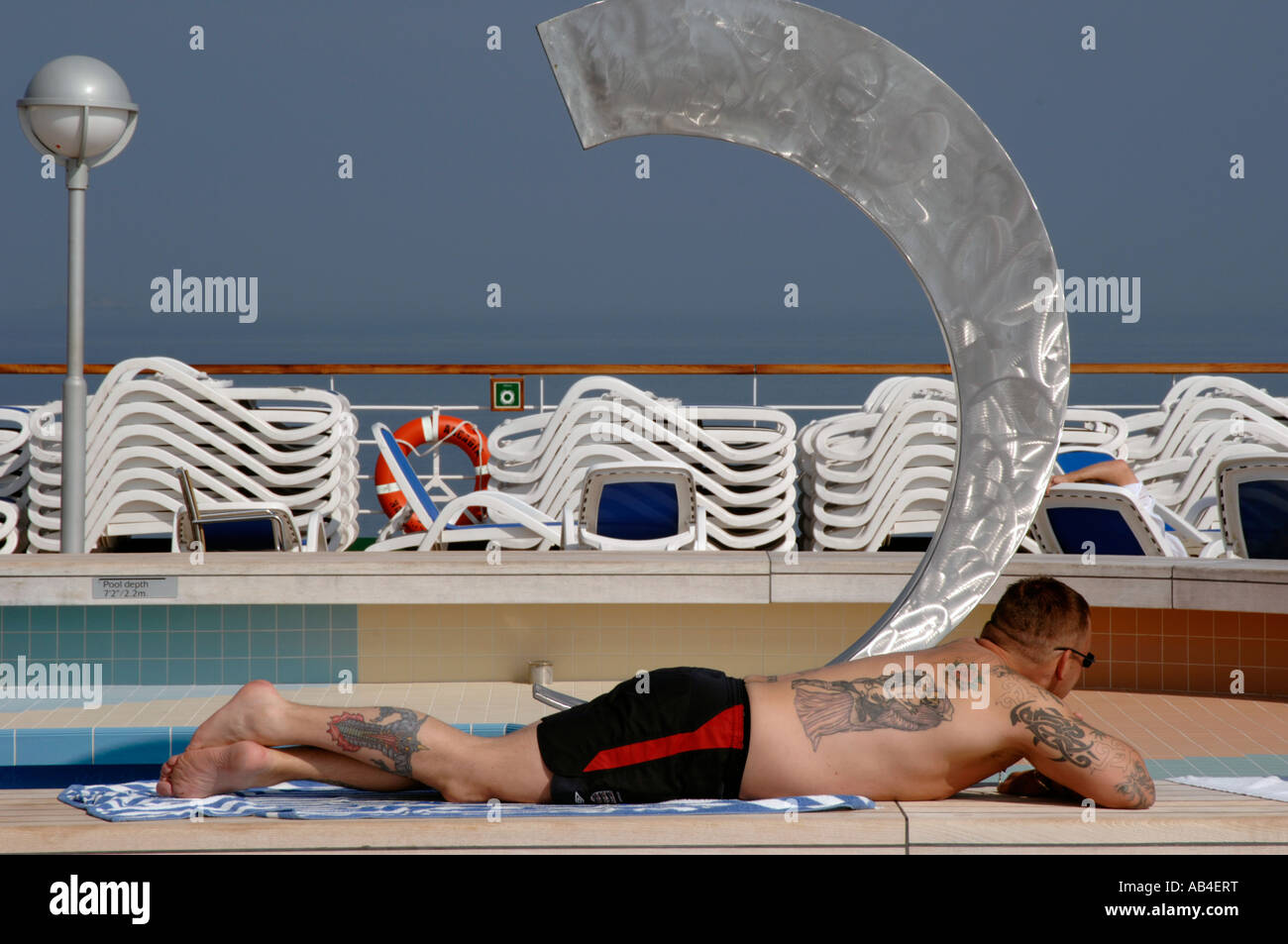 tattooed man sun bathing by a pool Stock Photo